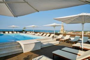 uma piscina com cadeiras brancas e guarda-sóis em Hotel Fonzari em Grado