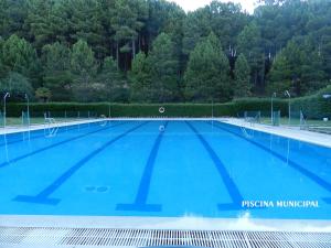 a large blue swimming pool with trees in the background at El Rencuentro Casa Rural de Gredos in Villarejo del Valle