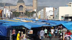 a group of people walking around a market with blue umbrellas at Pousada Mãe Padroeira in Aparecida
