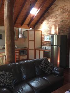 a living room with a black leather couch and a kitchen at Clover Cottage Country Retreat in Manjimup