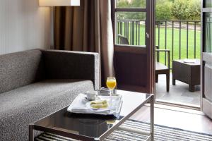 uma sala de estar com um sofá e uma mesa de vidro com uma bebida em Oca Vila de Allariz Hotel & Spa em Allariz