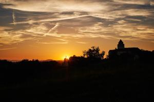 um pôr-do-sol com uma igreja e uma torre numa colina em LOISIUM Wine & Spa Resort Südsteiermark em Ehrenhausen