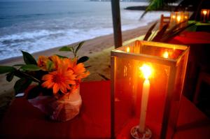 a candle and a vase of flowers on a table near the beach at Dilena Beach Inn in Tangalle