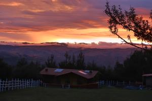 a house on a hill with a sunset in the background at The Lazy Dog Inn a Mountain Lodge in Huaraz