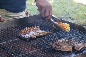 a person cooking meat and corn on a grill at Villa Tao in Tabanan