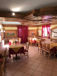 ブレントーニコにあるHotel Sole del Baldoのテーブルと椅子、赤いカーテンが備わるレストラン