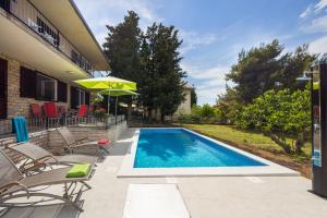 a swimming pool with chairs and an umbrella next to a house at Villa Amalia in Murter
