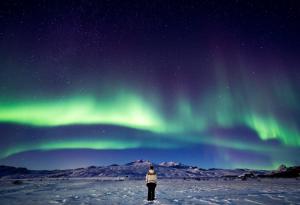 a person standing in the snow under the northern lights at Volcano Huts Þórsmörk in Thorsmork