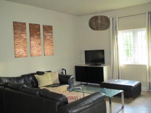 ein Wohnzimmer mit einem schwarzen Ledersofa und einem TV in der Unterkunft Villa De Alisha in Blue Bay