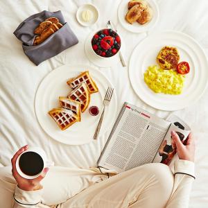 a person sitting on a bed reading a book and eating breakfast at Fontainebleau Miami Beach in Miami Beach