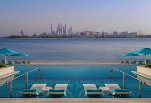 a swimming pool with chairs and umbrellas next to the water at The Retreat Palm Dubai MGallery by Sofitel in Dubai
