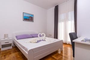 a white bedroom with a bed and a chair at Apartments Neve in Marina