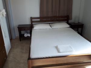 a bed with a wooden frame and white sheets at Angelos Rooms in Irakleia