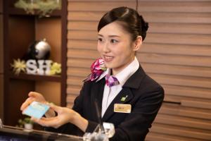 a woman in a suit and bow tie holding a card at Super Hotel Ogaki Ekimae in Ogaki