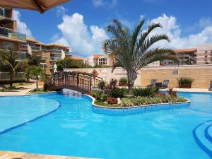 a large blue swimming pool with a palm tree and buildings at Condomínio Palm Beach in Aquiraz
