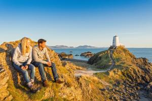 una pareja sentada en una roca cerca del océano con un faro en The Beach Motel, en Trearddur