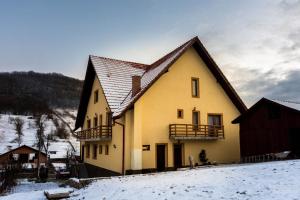 a large yellow house with a brown roof in the snow at Pensiunea Maria-Elena in Ponoarele