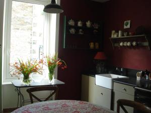eine Küche mit einem Tisch und einem Fenster mit Blumen darauf in der Unterkunft Maison d'Hôtes Augès in Tréguier