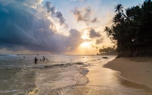 a group of people standing in the water at the beach at Rockside Cabanas Hotel in Unawatuna