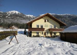 une maison dans la neige avec des montagnes en arrière-plan dans l'établissement Landhaus Tirol, à Presseggersee