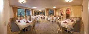 un restaurante con mesas y sillas blancas y ventanas en Hotel Sonne, en Tux