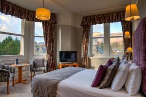 una camera da letto con un grande letto con finestre e televisore di Keswick Country House Hotel a Keswick