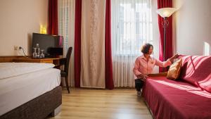 Hotel Am Schloss في آلتزي: امرأة جالسة في غرفة الفندق تطل من النافذة