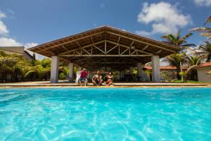 a group of people sitting under a pavilion over a swimming pool at Pousada Cabanas de Búzios in Nísia Floresta