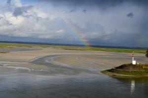 a rainbow over a beach with a lighthouse in the water at Hotel Les Pilotes in Saint-Valery-sur-Somme