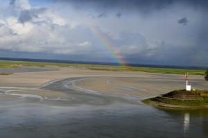 un arc-en-ciel sur une plage avec un phare dans l'eau dans l'établissement Hotel Les Pilotes, à Saint-Valery-sur-Somme