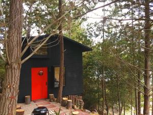 a black house with a red door in the woods at La Quinta Glamping - Lago de Tota in Cuítiva