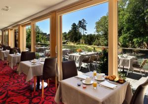 un restaurante con mesas, sillas y ventanas grandes en Hotel Spa Restaurant Domaine du Moulin, en Ensisheim