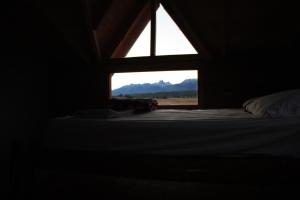 ventana en una habitación oscura con cama y montañas en Los Tres Picos en Cholila