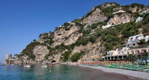 a beach with chairs and buildings and a mountain at Hotel Pupetto in Positano