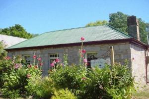a stone building with pink flowers in front of it at Colonial Cottages of Ross in Ross