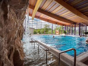 a swimming pool with a waterfall and people in it at Hotel Restaurant Waldmühle in Wolkenstein