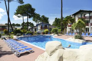a swimming pool with lounge chairs and a resort at Résidence Odalys Les Greens du Bassin in Gujan-Mestras