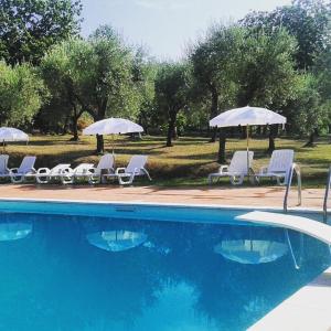 a swimming pool with white chairs and umbrellas at La Masseriola agriturismo in Caianello Vecchio