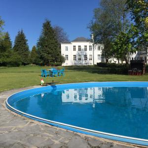 a large blue swimming pool in front of a white house at Holiday Home Manoir des Sarts in Cul-des-Sarts