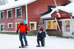 two people on skis in the snow in front of a house at Kuerkievari KuerHotel in Äkäslompolo