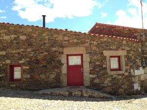 un edificio de ladrillo con una puerta roja y dos ventanas en Palheiro do Castelo - Pátio, en Sabugal