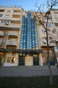ein hohes Gebäude mit einem Baum davor in der Unterkunft Apartman Gold in Novi Sad