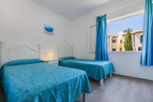 a bedroom with two beds and a window with blue curtains at Apartamentos Don Miguel in Port de Pollensa