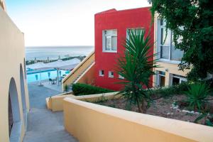 a red building with a palm tree in front of it at Saint Catherine Hotel in Pythagoreio