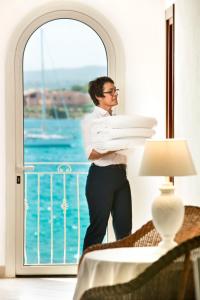 un hombre parado frente a una ventana sosteniendo una pila de platos en Gabbiano Azzurro Hotel & Suites, en Golfo Aranci