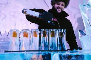 a man is standing behind a table with champagne glasses at Hotel de Glace in Saint-Gabriel-De-Valcartier