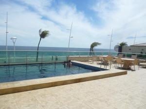 a swimming pool with a table and chairs and the ocean at Flat no Farol in Salvador