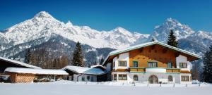 ein Haus im Schnee mit Bergen im Hintergrund in der Unterkunft Ferienwohnung Simair in Sankt Ulrich am Pillersee