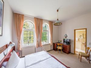 a bedroom with a bed and a desk and two windows at Hotel Villa Raueneck in Bad Saarow
