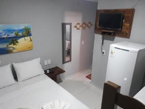 a bedroom with a white bed and a tv at Suítes Canaã in Canoa Quebrada